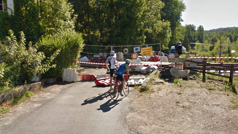 Google Street View showing two cyclists surprised on a small country road closed at railway crossing.